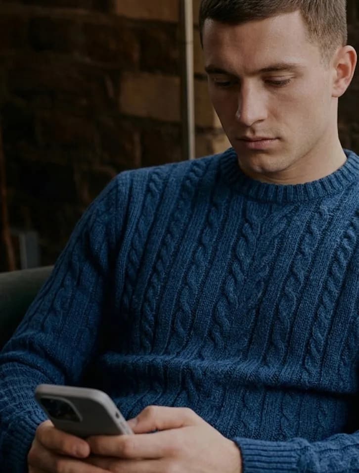 Man in a blue knit sweater checking his portfolio on a phone